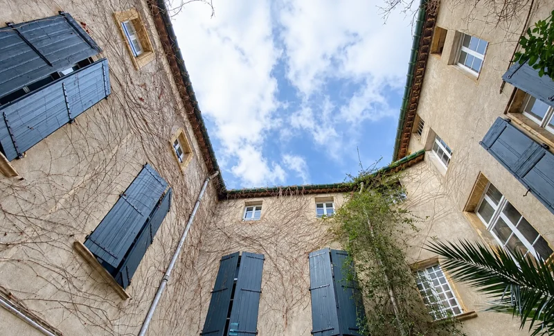 Cour intérieure de l’Hôtel Bénavent à Narbonne, avec façades en pierre et volets bleus