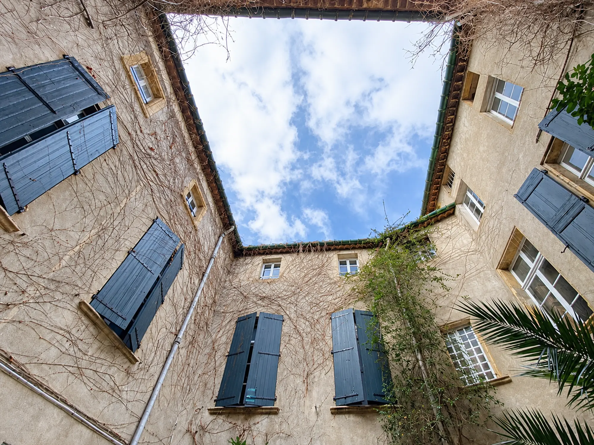 Cour intérieure de l’Hôtel Bénavent à Narbonne, avec façades en pierre et volets bleus